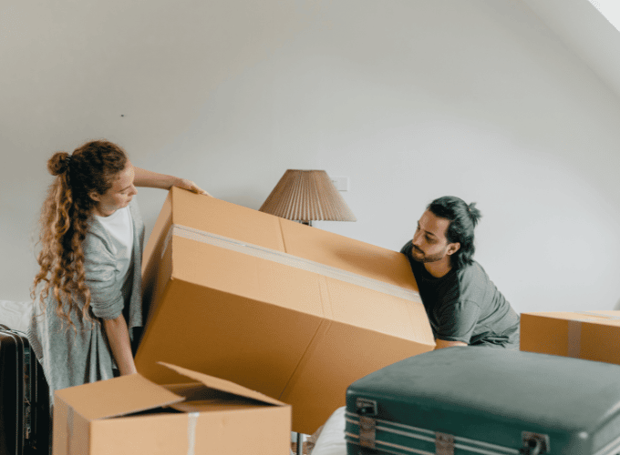 a man and a woman lifting a box while moving to a bigger house
